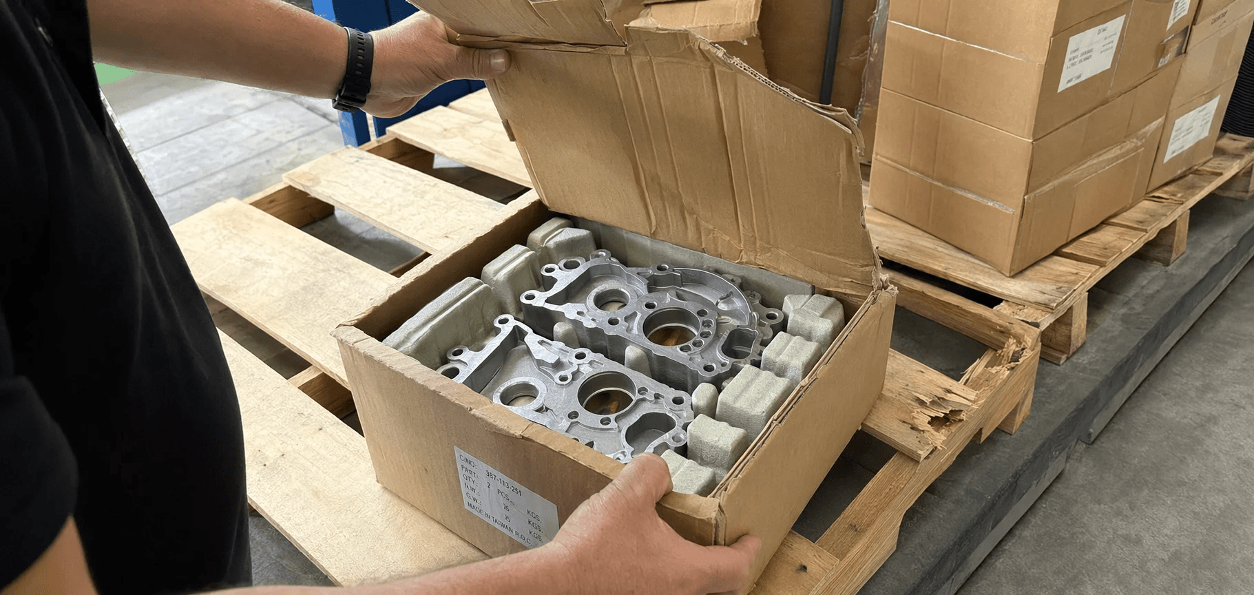 A Naisitong engineer inspecting three pallets of air-freighted aluminum die-cast parts with varying degrees of packaging damage at a German Tier-1 customer warehouse, checking each part's condition one by one.