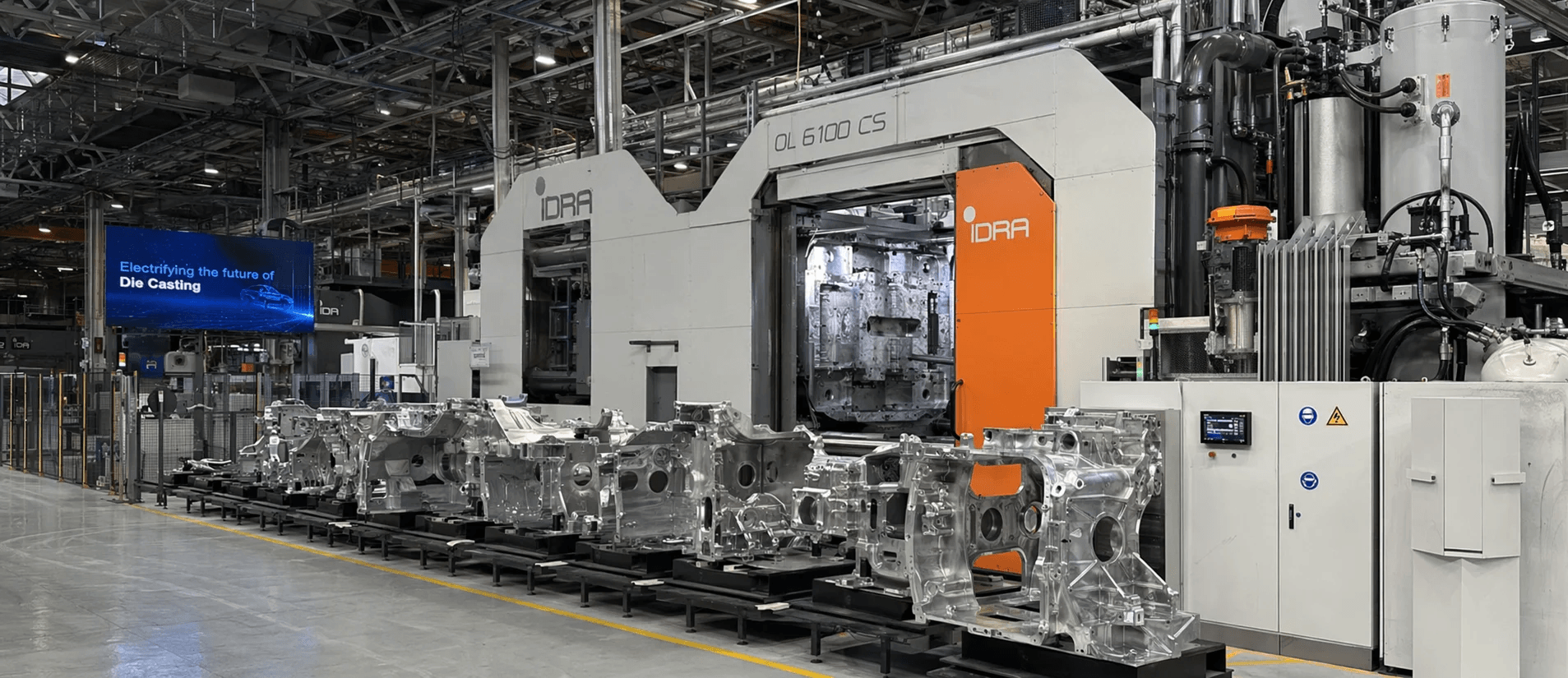 A modern die-casting cell with a large-scale integrated giga-press producing an aluminium structural component for an electric vehicle, illuminated by molten metal glow